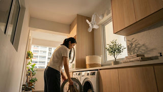 Woman doing laundry under a white 360 wall fan in a compact Singapore service yard