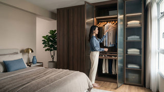 Woman organising clothes inside a wood wardrobe with glass doors in a 5-room HDB master bedroom.