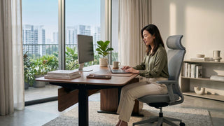Woman working at an adjustable study table with monitor and laptop in a modern Singapore apartment home office.