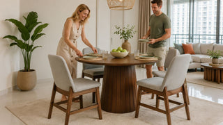 White couple setting a round wooden dining table in a bright modern Singapore apartment dining area.