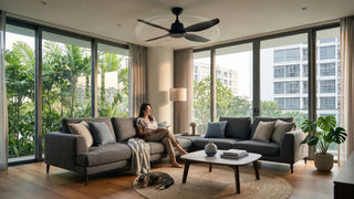 Black Amasco-style ceiling fan in a modern Singapore condo living room with grey sofa, large windows, indoor plants and a relaxed reading corner.