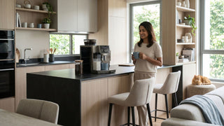 Woman holding coffee beside an automatic coffee machine in a modern Singapore open-plan kitchen.