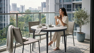 Woman enjoying coffee at a round balcony dining table in a Singapore condo with outdoor chairs and city views.