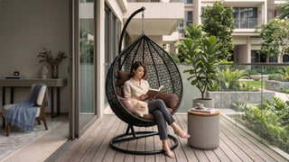 Woman reading with a cat in a balcony swing chair on a modern Singapore condo balcony