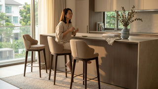 Woman sitting at a kitchen island with upholstered bar stool chairs in a bright Singapore home.