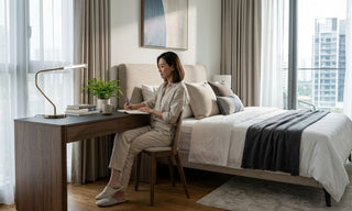 Woman writing at a bedside study table in a modern Singapore bedroom with neutral decor and natural light