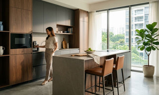 Woman using a built-in microwave oven in a modern Singapore condo kitchen with wood cabinetry and island seating.