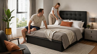 Modern black upholstered bed frame in a bright Singapore bedroom with a couple arranging pillows and bedding.