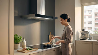 Woman cooking under a black kitchen hood above an induction hob in a bright HDB-style kitchen