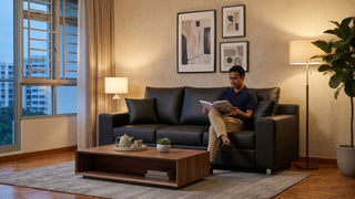 Man reading on a black lounge sofa in a cosy evening living room with warm lighting