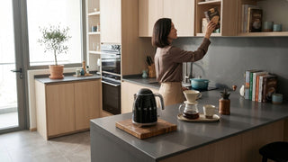 Black SMEG kettle beside pour-over coffee setup on a modern kitchen island with warm wood cabinetry