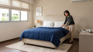 Woman arranging a blue comforter on a cream upholstered bed in a simple modern Singapore bedroom
