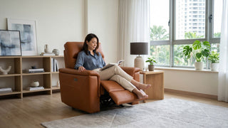 Woman reading on a brown leather single recliner sofa in a bright Singapore living room with window plants and neutral decor.