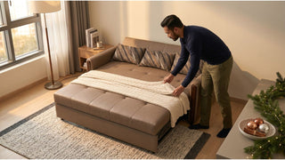 Man arranging a blanket on a brown sofa bed in a cosy Singapore living room ready for holiday guests