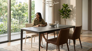 Woman seated at a dark sintered stone dining table in a bright Singapore condo dining area with balcony windows and upholstered chairs.