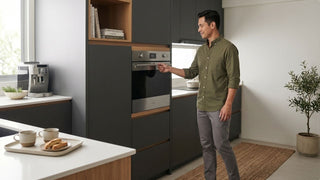 Man checking a built-in combo oven in a compact Singapore kitchen with dark cabinets and wood accents