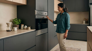 Woman using a built-in oven in a modern Singapore kitchen with dark cabinets and warm countertop styling