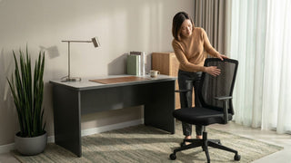 Woman checking a mesh office chair beside a grey desk in a Singapore work-from-home space