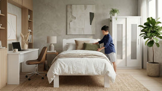 Boy arranging pillows on a white bed in a spacious children’s room with wardrobe and study desk