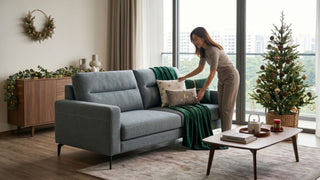 Woman arranging cushions on a grey sofa bed in a Singapore living room decorated for Christmas