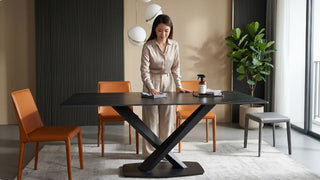 Woman cleaning a black dining table in a modern Singapore dining room with orange chairs and neutral styling