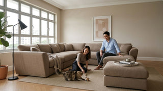 Couple relaxing with a cat near a brown sectional sofa and ottoman in a bright home