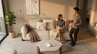 Couple arranging a cream 3-seater sofa with coffee table, rug, plant, and warm evening light in a Singapore condo