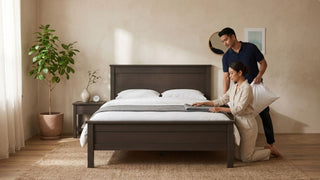 Couple styling a dark wood bed frame in a warm modern Singapore bedroom with neutral bedding, rug, and indoor plant