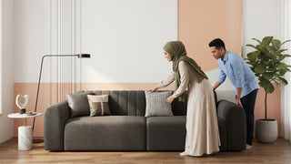 Couple styling cushions on a grey fabric sofa in a modern Singapore living room with warm walls, wood flooring, and indoor plant