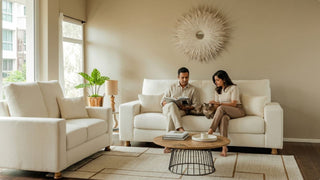 Couple reading on a cream sofa with a cat in a warm Singapore home with matching armchair