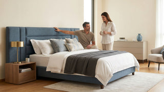 Couple viewing a blue upholstered bed frame in a bright Singapore bedroom with wooden bedside table and neutral decor.