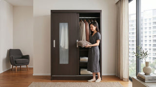 Woman storing folded clothes in a dark sliding wardrobe in a bright Singapore bedroom with city window views