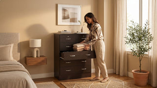 Woman organising folded clothes in a dark wood dresser cabinet in a cosy bedroom