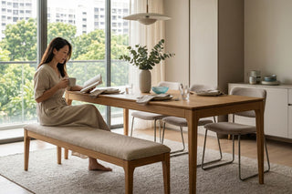 Woman reading beside a wooden dining set with bench in a bright Singapore condo dining area.