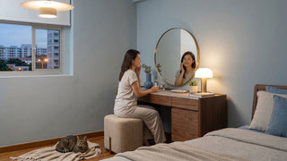 Woman using a wooden dressing table with round mirror in a resale HDB bedroom, showing stool clearance beside the bed.