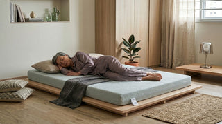 Elderly woman resting on a low tatami mattress with wooden platform in a calm Singapore bedroom