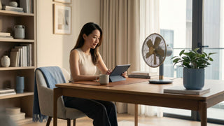 Woman using a tablet beside an electric table fan in a bright Singapore home office.