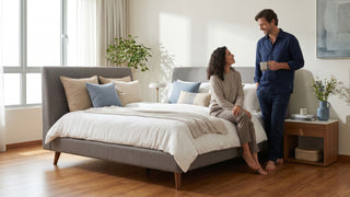 European fabric bed frame with grey upholstered headboard in a bright Singapore bedroom with a couple and wooden bedside table.