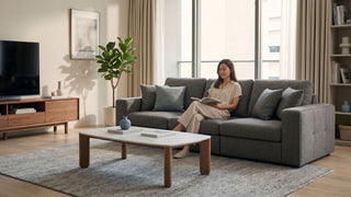 Woman reading on a grey fabric sofa in a bright Singapore living room with coffee table, TV console and soft neutral decor.