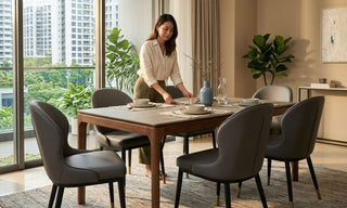 Woman setting a modern dining table with grey faux leather dining chairs in a bright Singapore condo dining room.