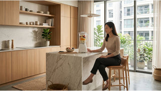 Woman using a food blender on a marble kitchen island in a bright Singapore home
