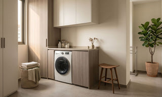 Front-load washing machine fitted into a warm HDB laundry corner with wood cabinets, countertop storage, laundry basket, and natural light.