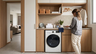 Front-load washing machine in a compact Singapore HDB laundry area with wood cabinetry and folded towels