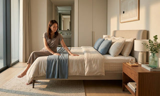 Woman testing a mattress in a warm modern Singapore bedroom with neutral bedding and blue accents.