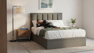 Man resting on a grey double bed frame in a minimalist Singapore bedroom with bedside table and floor lamp
