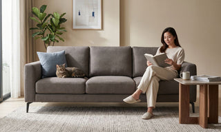 Cat resting on a grey fabric sofa in a Singapore home while a woman reads beside it