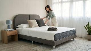 Woman styling pillows on a grey pocketed spring mattress with a cat resting on the bed