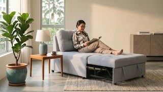 Woman reading on a grey single sofa bed in a bright Singapore living room with side table and indoor plant