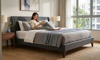 Woman reading on a grey upholstered bed frame in a bright Singapore HDB bedroom