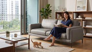 Woman reading on a grey half leather sofa in a Singapore condo living room with balcony and cat